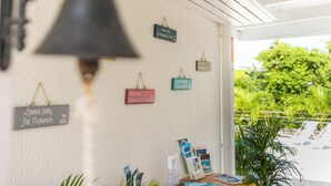 A wall with hanging signs and a bell, a table with books and a menu, and a view of greenery outside.