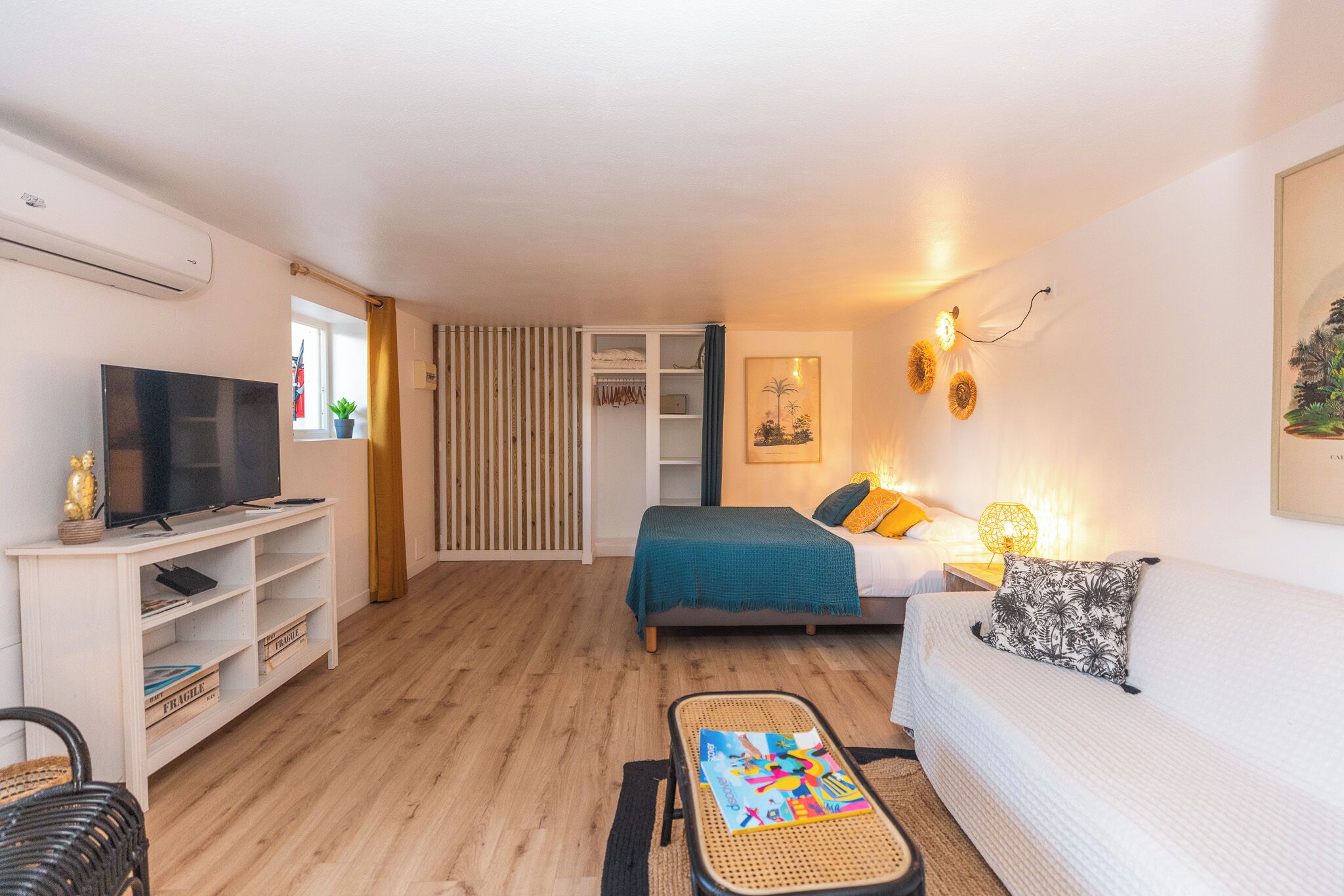Ein modernes, helles Zimmer mit einem Bett, einem Schlafsofa, einem Fernseher und einem kleinen Tisch.