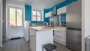 A modern kitchen with a central island, white cabinets, a stainless steel refrigerator, and a window with a view of the outside. - Le Cancalais - Port - Wifi - Plage (Cancale)