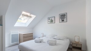 A modern bedroom with a skylight, a bed with white linens, a wooden dresser, and two framed artworks on the wall. - Le Cancalais - Port - Wifi - Plage (Cancale)