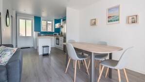 A modern kitchen with white cabinets, a microwave, and a sink. There is a dining area with a wooden table and four chairs. - Le Cancalais - Port - Wifi - Plage (Cancale)