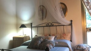 Ein Bett mit Baldachin, ein Nachttisch, eine Lampe und ein kleiner Hocker.
