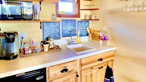 Una cocina con armarios de madera, lavavajillas, microondas y ventana con cortinas.