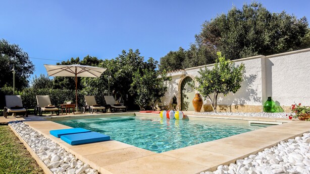 En swimmingpool med fliseterrasse, liggestole og en pergola med parasol.