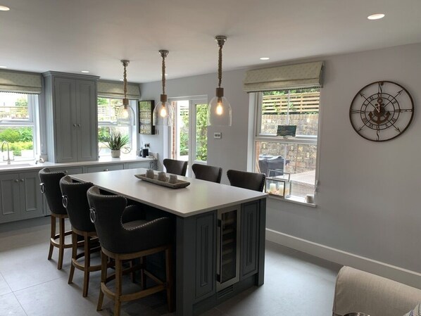 A kitchen with a central island, bar stools, pendant lighting, and a clock on the wall.