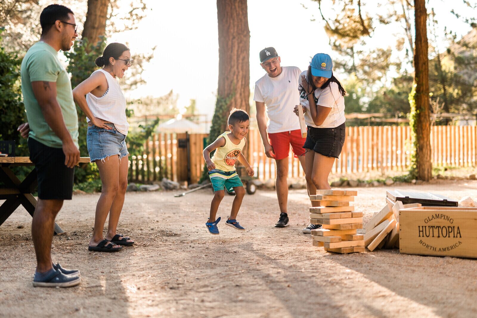 Un grupo de personas jugando Jenga al aire libre, en un terreno de tierra con vallas de madera al fondo.