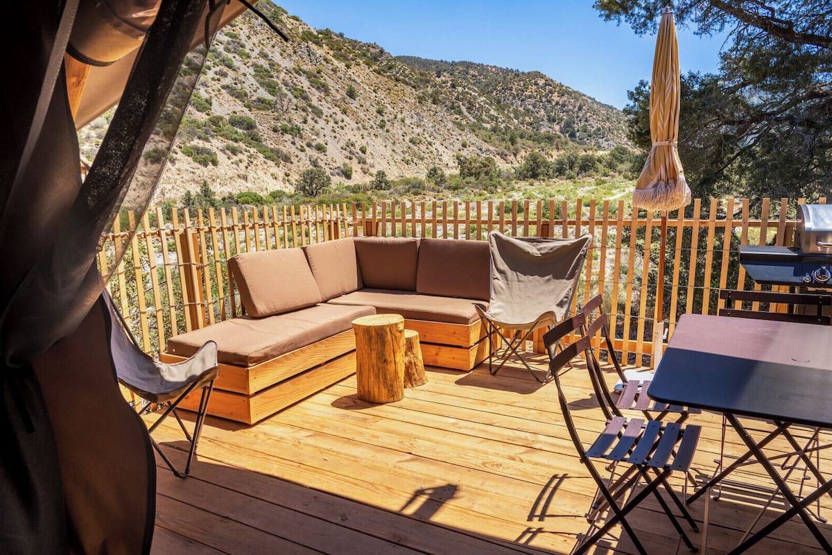 Una terraza de madera con un sofá modular, una silla plegable, una mesa y una parrilla.