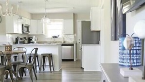 A modern kitchen with white cabinets, a dining area with a table and chairs, and a TV on a stand.