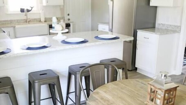 A modern kitchen with white cabinets, a central island with stools, and pendant lighting.