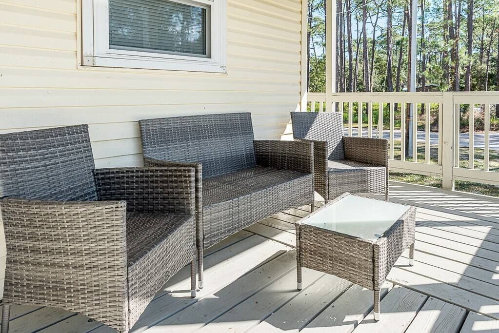 A wicker sofa set with a glass-top coffee table on a wooden deck.