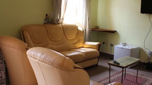 Un salon avec un canapé beige, une petite table, un téléviseur et un réfrigérateur.