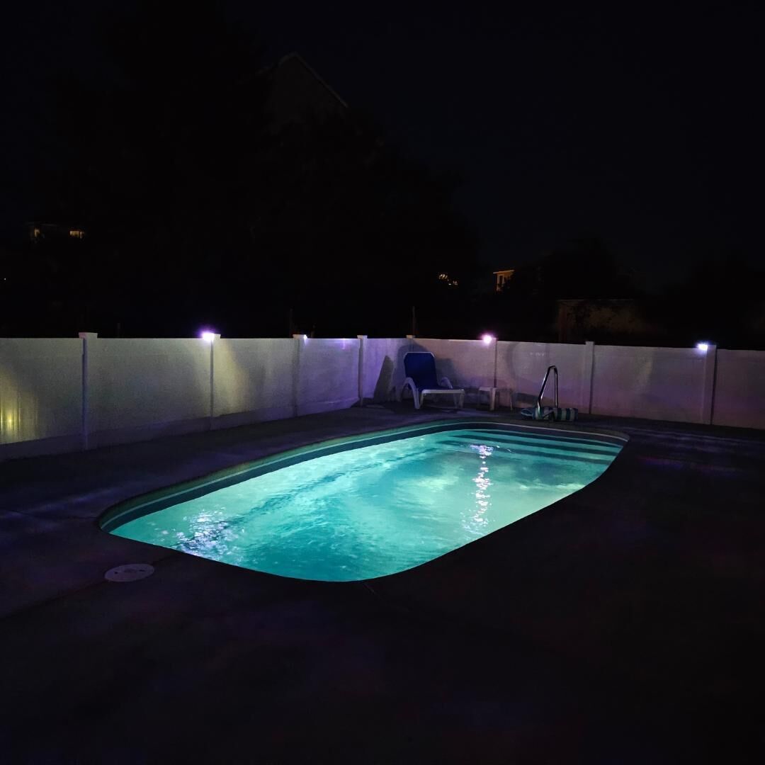 A swimming pool at night with a few lounge chairs and a small staircase leading into the water.