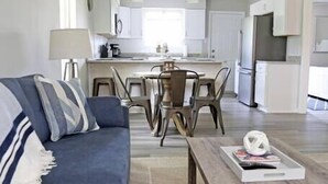 A modern living room with a blue sofa, a wooden coffee table, and a dining area with chairs and a table. - Gulf Coast Condos on the Sand Dunes - 202 (Dauphin Island)