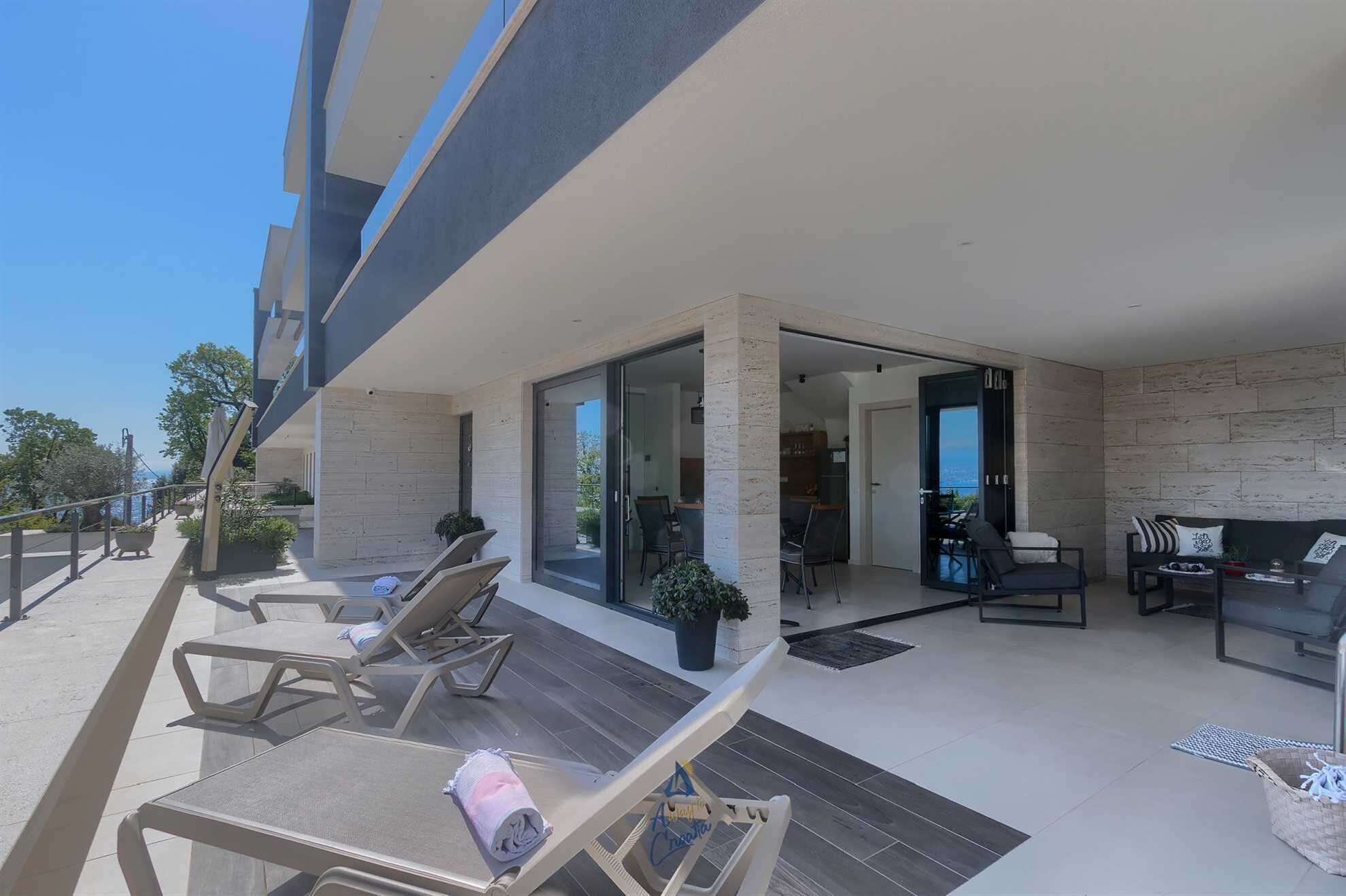 Un espace de vie extérieur moderne, doté de fauteuils de salon, d’une table à manger et offrant une vue sur la mer.