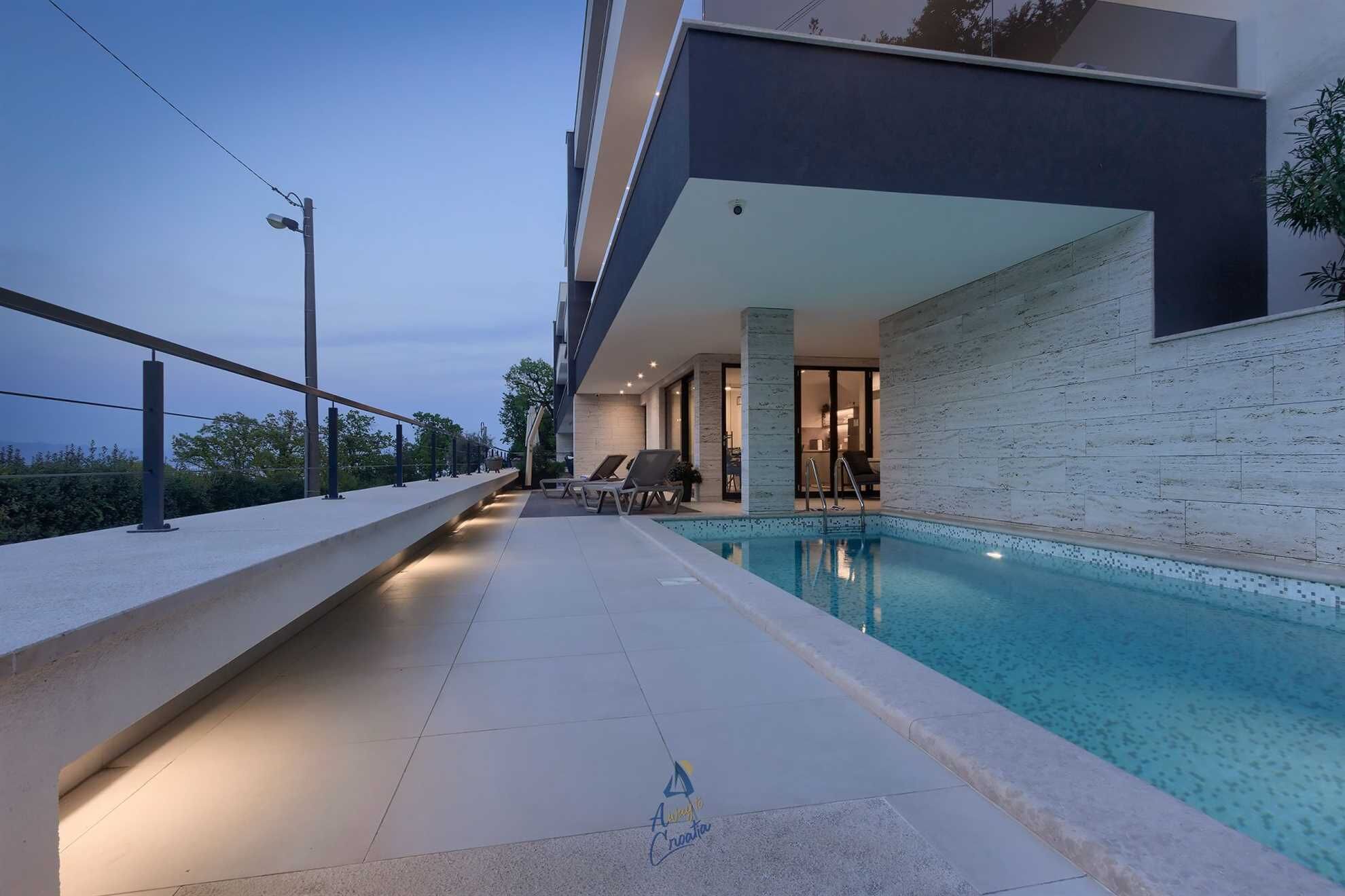 Un área de piscina exterior moderna con vistas despejadas al mar, una zona de estar cubierta y un camino bien iluminado.
