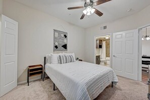 A bedroom with a bed, a ceiling fan, a wall-mounted artwork, and a door leading to another room.