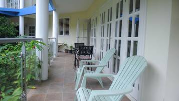 A covered outdoor area with chairs and a table, potted plants, and a view of the building's interior.