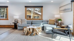 Una sala de estar moderna con un sofá modular, una mesa de centro de madera y vistas a un paisaje nevado a través de un ventanal grande.