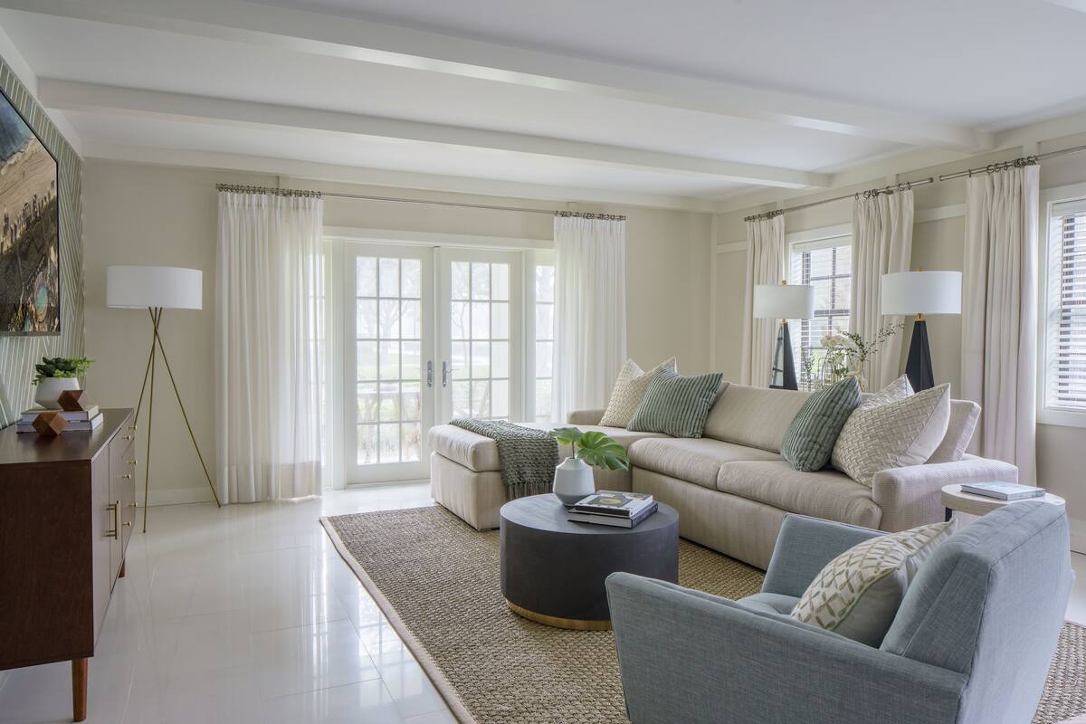 A modern living room with a sofa, armchairs, a coffee table, and a side table. There is a floor lamp, a painting on the wall, and a window with curtains.