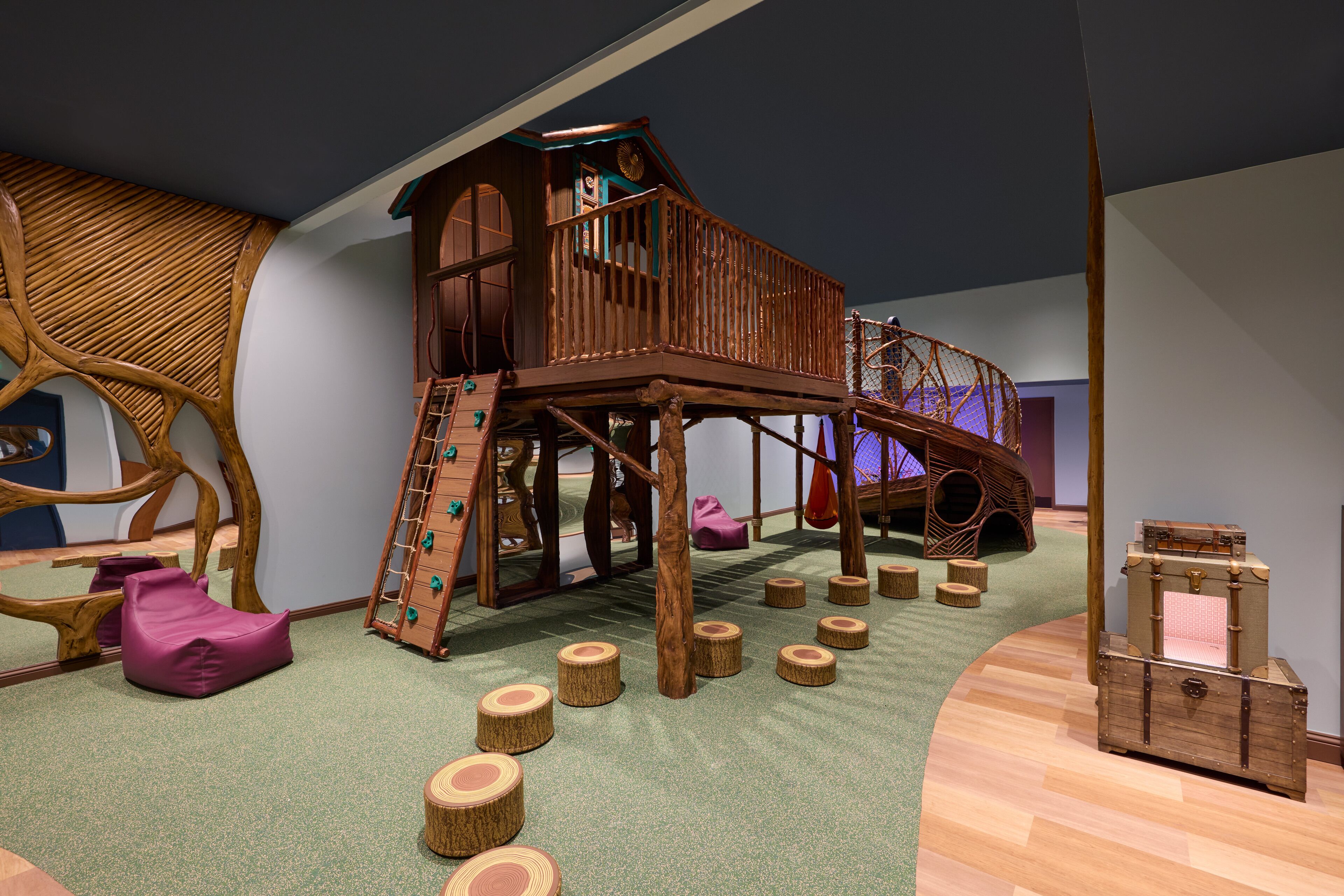 A play area with a wooden playhouse, a slide, and a soft play mat.