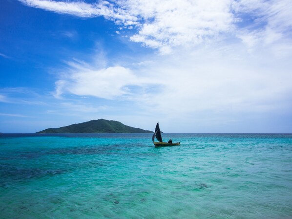 A clear view of turquoise waters with a small boat and a person in a hat.