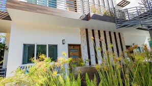 Una moderna casa a due piani con un balcone, una facciata in pietra e un giardino curato con diverse piante.