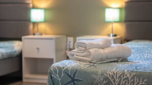 Ein ordentlich bezogenes Bett mit einem Stichmuster in Form von Meeressternen, ein Stapel gefalteter Handtücher und zwei Nachttische mit grünen Lampenschirmen.