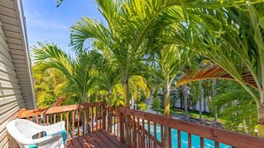Eine Holzterrasse mit einem weißen Korbstuhl, umgeben von Palmen und einem Pool.