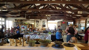 A spacious indoor venue with high ceilings and exposed beams, featuring tables with pottery and various items, and a crowd of people engaged in activities. - Desert Oasis Campground (McNeal)