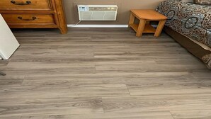 A room with a herringbone-patterned wooden floor, a wooden dresser with drawers, a small wooden table, and a patterned sofa. - Desert Oasis Campground (McNeal)