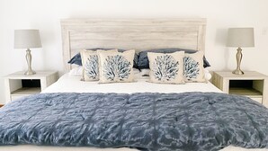 Een bed met een blauwe geweven deken, twee nachtkastjes met lampen, en decoratieve kussens met een blauw-wit patroon.