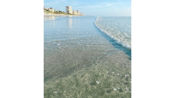 Een strand met helder ondiep water en een zicht op gebouwen aan de kust.