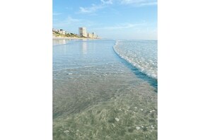 A beach with clear shallow waters and a distant view of buildings on the shore. - Private oasis w/pool near Daytona (Port Orange)