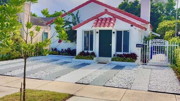 A small, single-story house with a red-tiled roof, a front door, and a gated entrance. - Beautiful Chic Home Near Coconut Grove & Brickell (Miami)