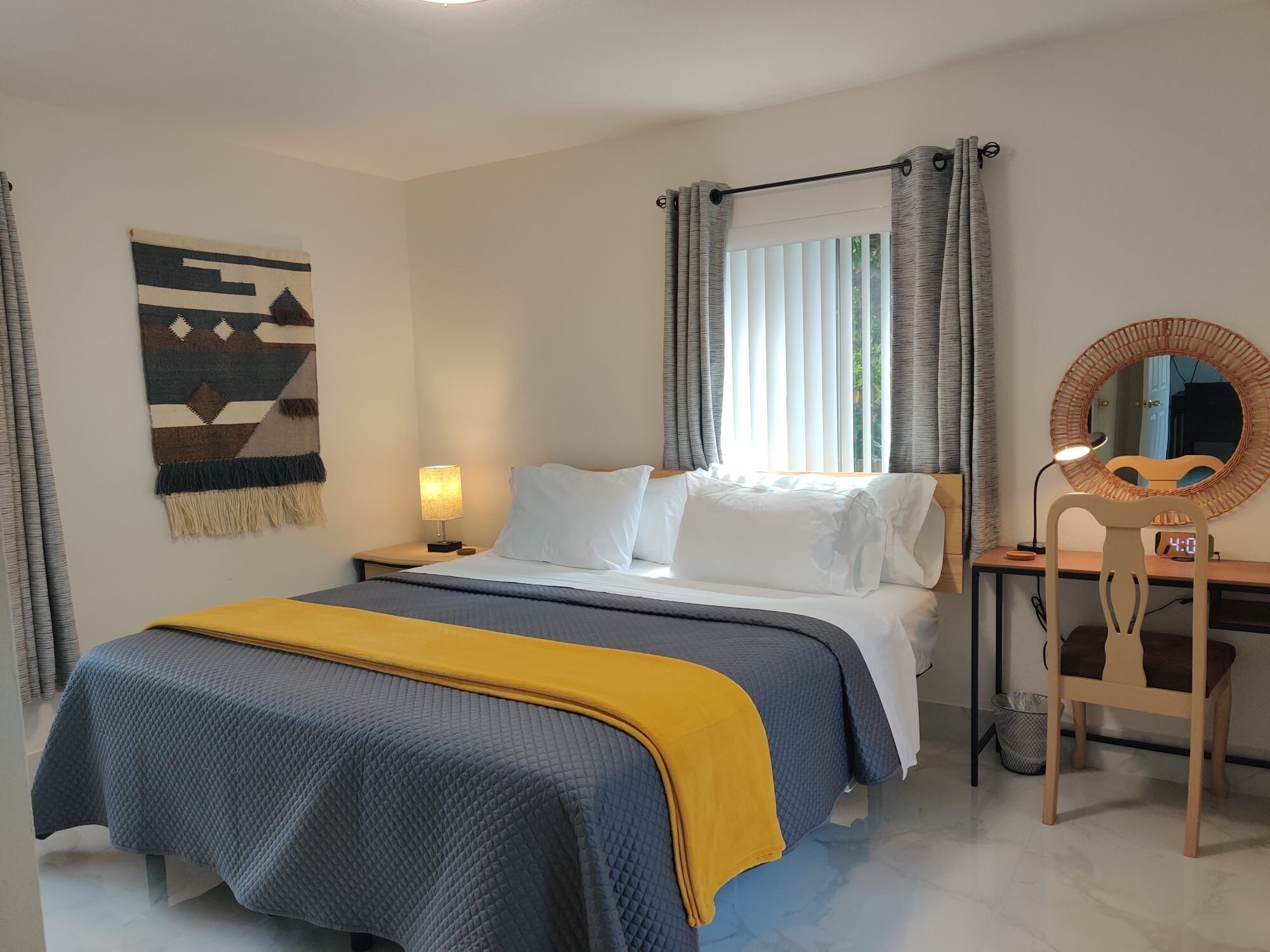 Un dormitorio con cama, mesita de noche, lámpara, silla y espejo en la pared.