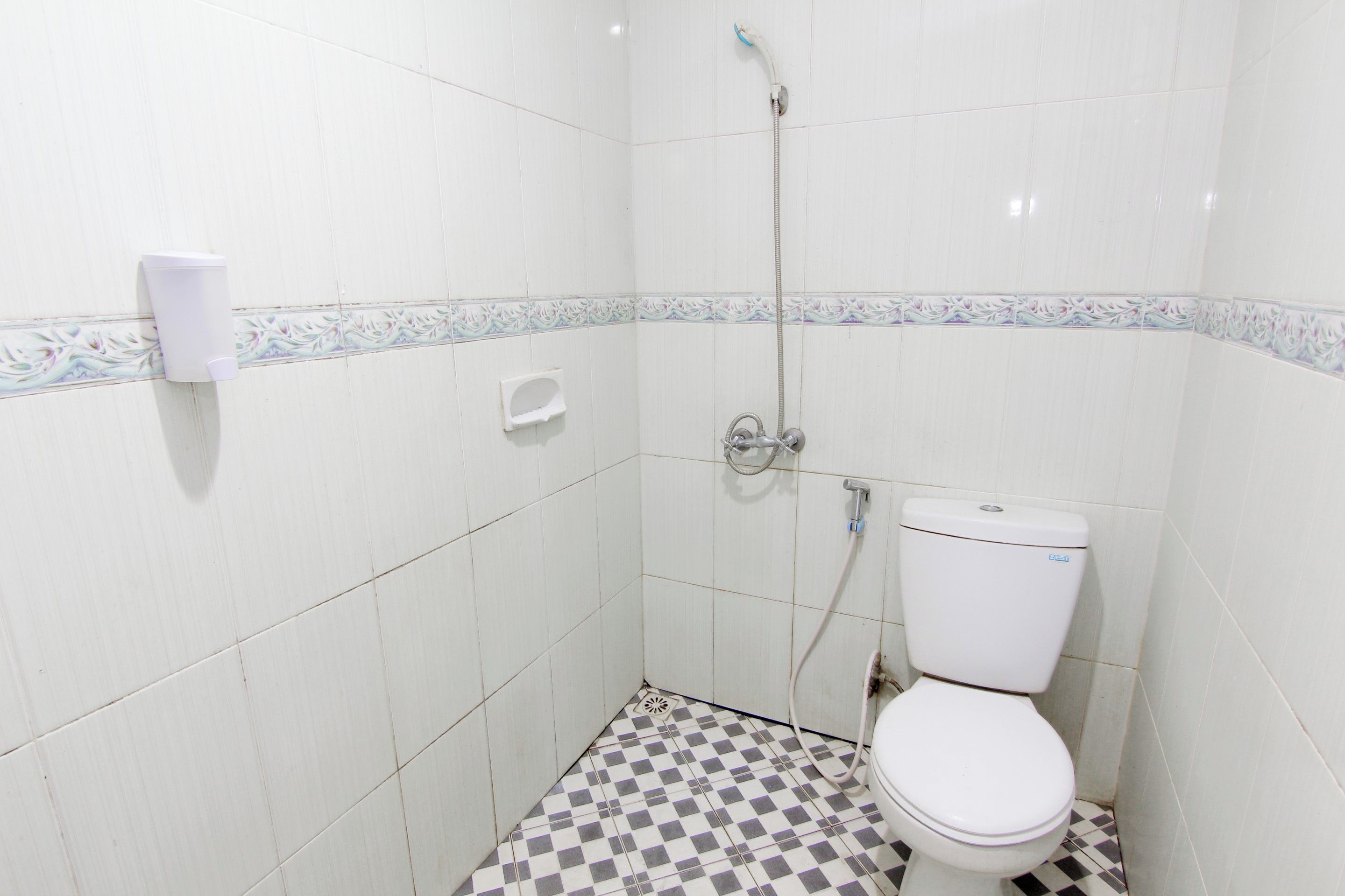 A small, tiled bathroom with a toilet, a shower, and a soap dispenser.