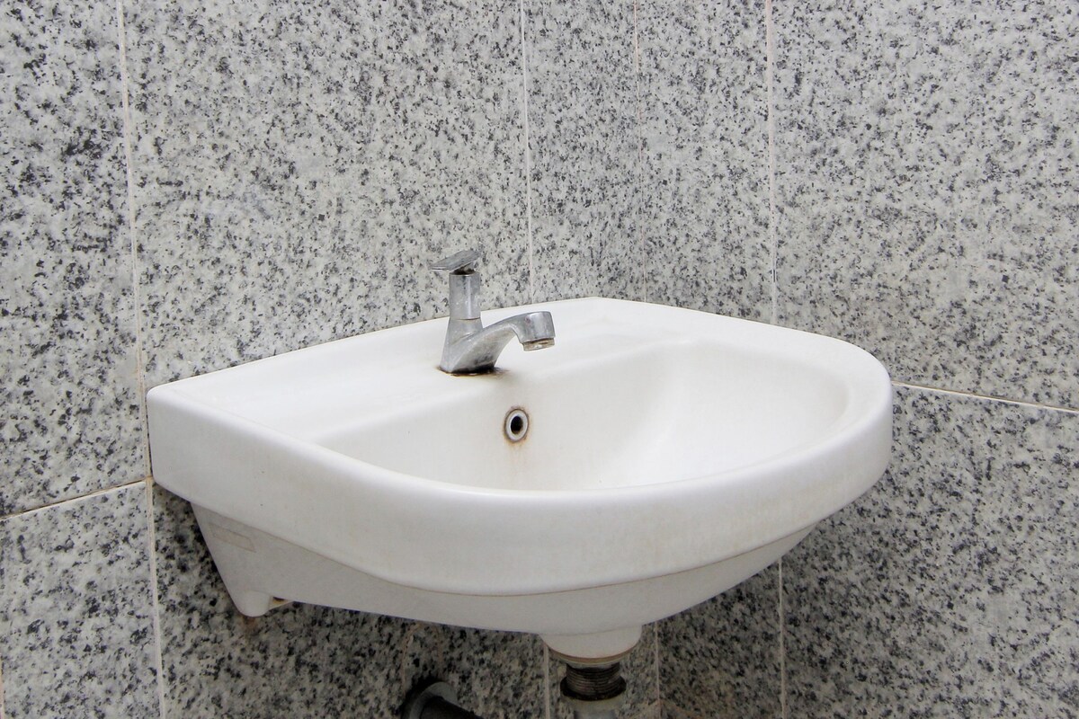 Un lavamanos blanco con un solo grifo, frente a una pared de azulejos con motas.