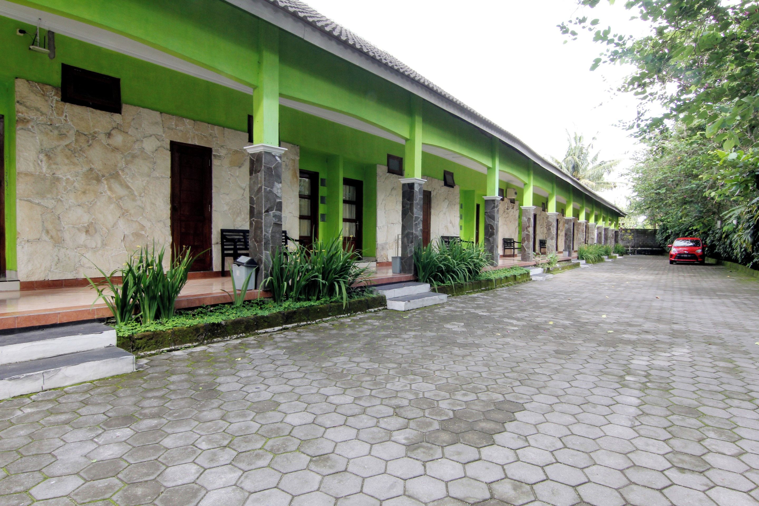 Un edificio con fachada verde, pavimento hexagonal y un automóvil rojo estacionado afuera.
