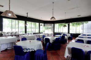 Ein Restaurant mit mehreren Tischen und Stühlen, großen Fenstern und hängenden Lampen.