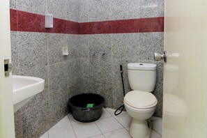 A small bathroom with a white sink, a toilet, and a black bucket on the floor. - Hotel Popi by Zuzu (Ngaglik)