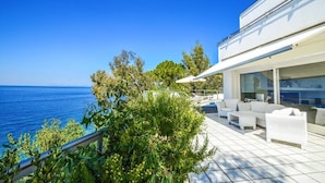 A modern outdoor patio with white furniture, a pool, and a view of the sea.