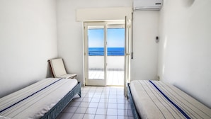 A hotel room with two beds, a balcony with a view of the sea, and an air conditioning unit.