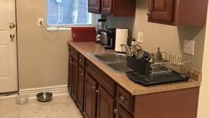 Une cuisine compacte avec des meubles en bois, un plan de travail en granit, un évier encastré et une fenêtre donnant sur un bâtiment en briques.
