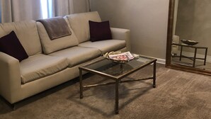Un salon avec un canapé beige, une table basse en verre, un lampadaire et un grand miroir.