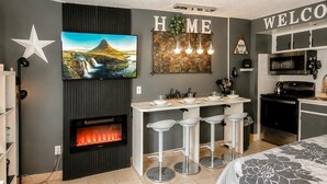 A modern kitchen with a built-in stove, bar stools, and a TV above the fireplace. - SC 2211: Chic Mountain Studio | Perfect for Summer Adventures (Snowshoe)