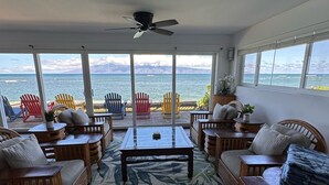 A spacious living room with a large glass table, comfortable seating, and a ceiling fan.