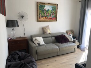 A living room with a grey sofa, a standing fan, a lamp, and a painting on the wall.