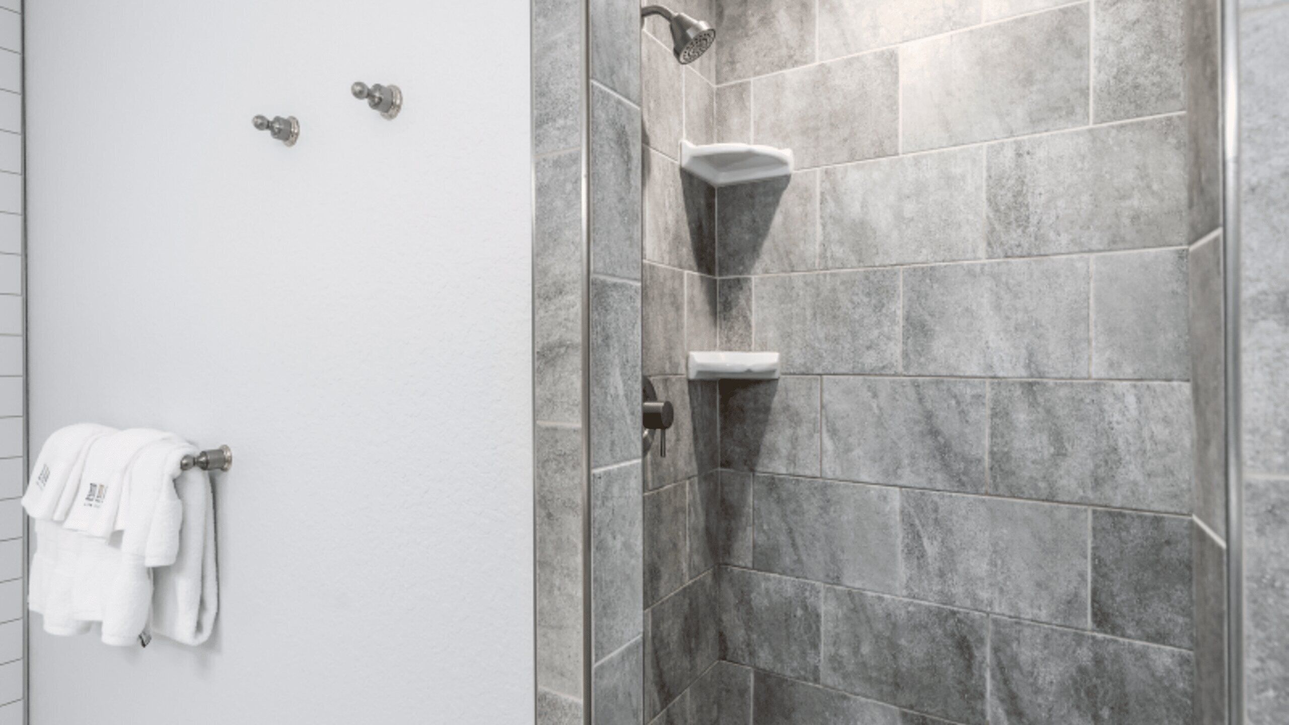 A shower area with grey tiles, a white towel rack with towels, and a showerhead.