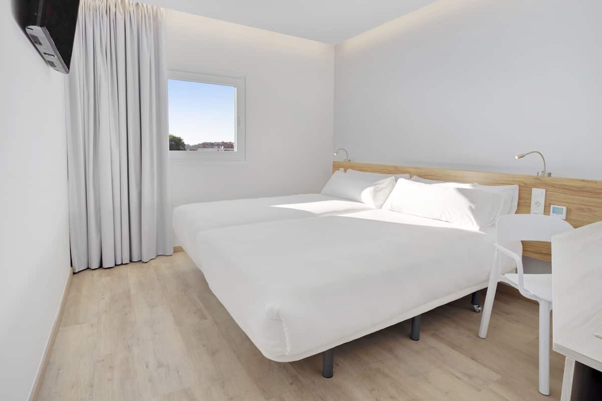 Una habitación de hotel moderna con una cama grande, una mesita de noche, una silla y una ventana con vistas.