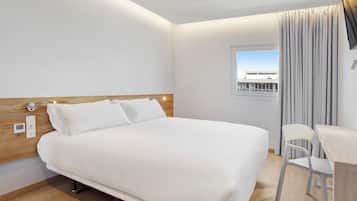 Een moderne hotelkamer met een groot bed, een houten hoofdeinde, een bureau met stoel, en een raam met gordijnen.
